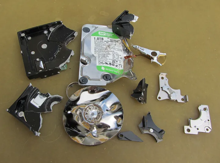 Photo d’origine : Disque dur éventré dont le plateau et les pièces mécaniques gisent en morceaux.