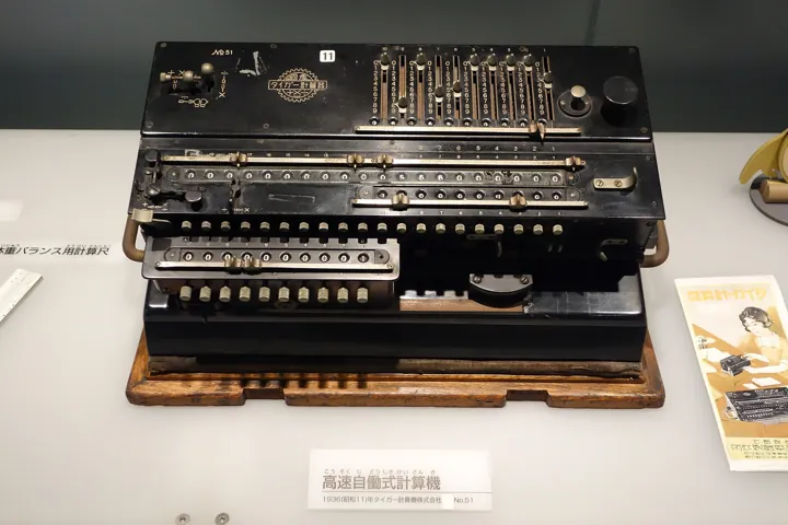 Photo d’origine : Calculatrice mécanique ancienne à leviers, à curseurs et à rangées de touches, exposée dans une vitrine.