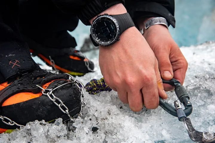 Photo d’origine : Mains d'un alpiniste refermant un mousqueton sur la corde, crampons aux pieds, sur la glace d'un glacier.