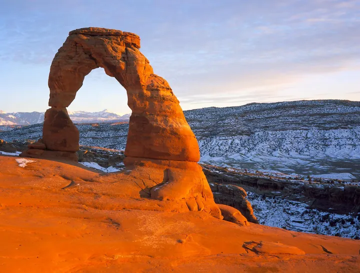Photo d’origine : Delicate Arch, arche de grès rouge qui encadre des montagnes enneigées au loin