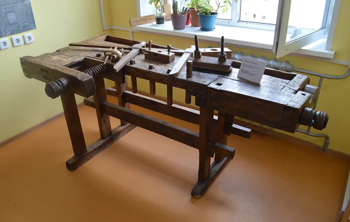Photo d’origine : Ancien établi de menuisier en bois, avec ses étaux à vis et ses outils posés dessus.
