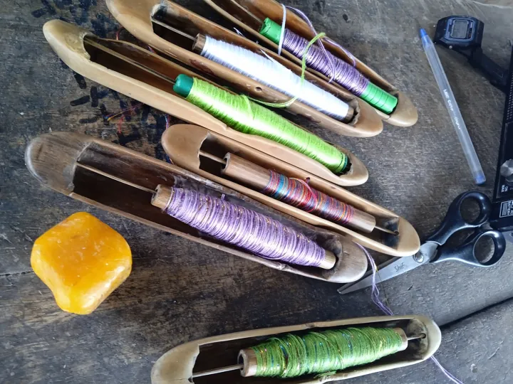 Photo d’origine : Navettes de tissage en bois garnies de fils de couleur, utilisées pour tisser le kente.