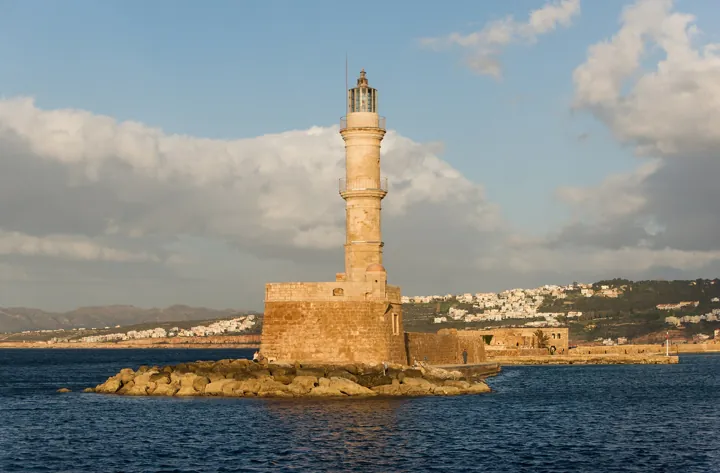 Photo d’origine : Un phare de pierre sur une jetée rocheuse, éclairé par le soleil du soir au-dessus de la mer.