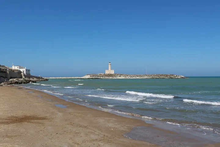 Photo d’origine : Le phare de Vieste, sur son îlot, vu depuis la plage au bord d'une mer calme.