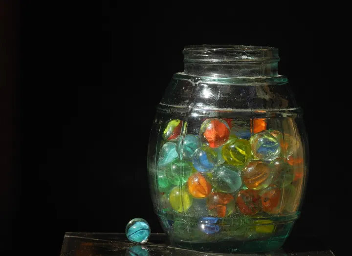 Photo d’origine : Un bocal de verre rempli de billes de couleurs diverses, sur fond noir.