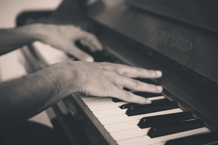 Photo d’origine : Les mains d'un pianiste posées sur les touches d'un piano, en noir et blanc.