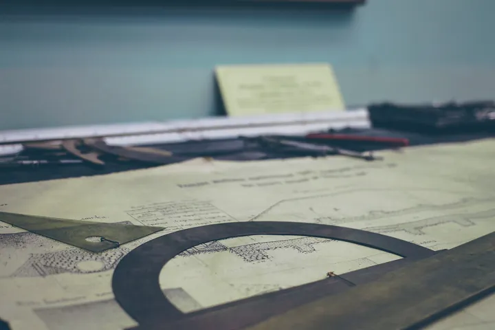 Photo d’origine : Un rapporteur, une équerre et un compas posés sur d'anciens plans dessinés.