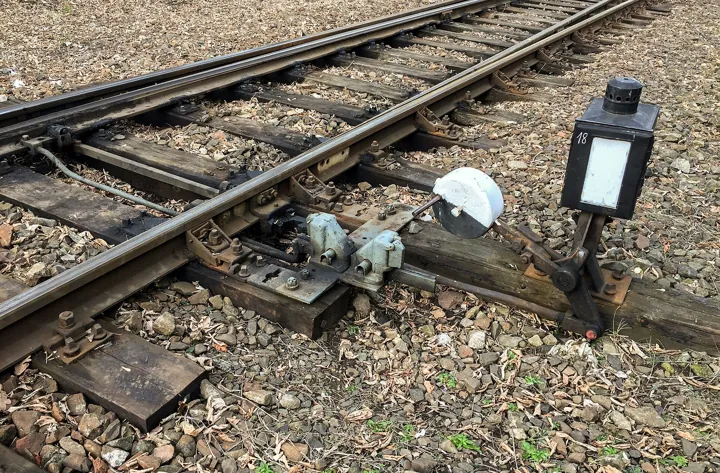 Photo d’origine : Aiguillage ferroviaire manœuvré à la main, où la voie se sépare en deux, avec sa lanterne de signalisation.