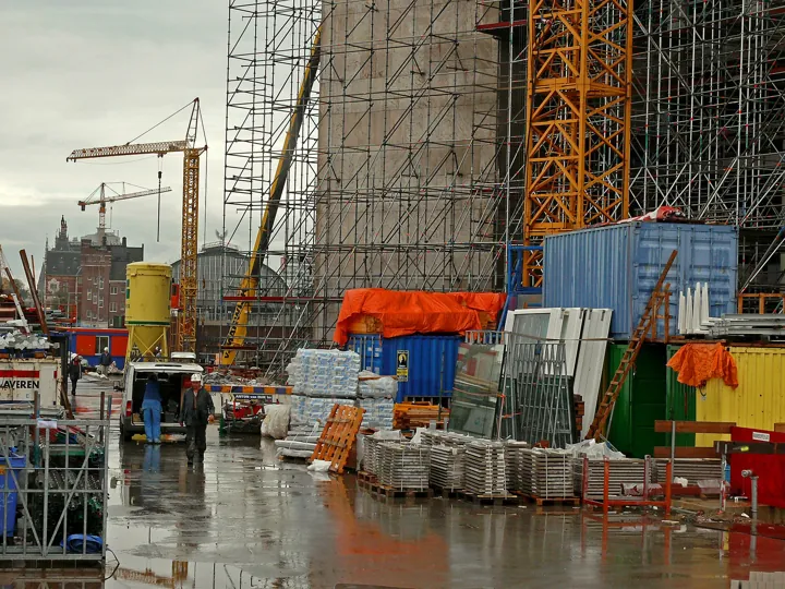 Photo d’origine : Chantier de construction enserré dans d'énormes échafaudages, avec grues et conteneurs de matériaux.