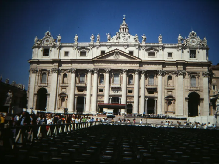 Photo d’origine : La façade de la basilique Saint-Pierre de Rome, sous un ciel bleu, avec la foule au pied des marches.