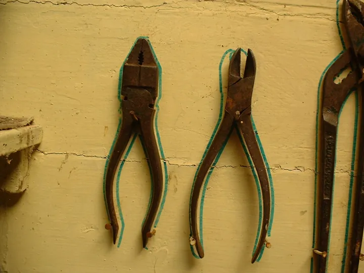 Photo d’origine : Pinces accrochées à un mur d’atelier, chacune entourée du contour tracé de sa place.