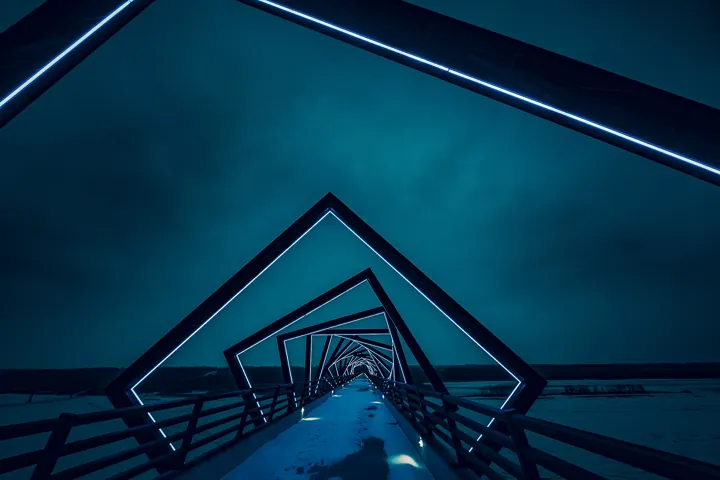 Photo d’origine : Passerelle de nuit, dont les cadres lumineux décalés forment un tunnel au-dessus d’une vallée enneigée.
