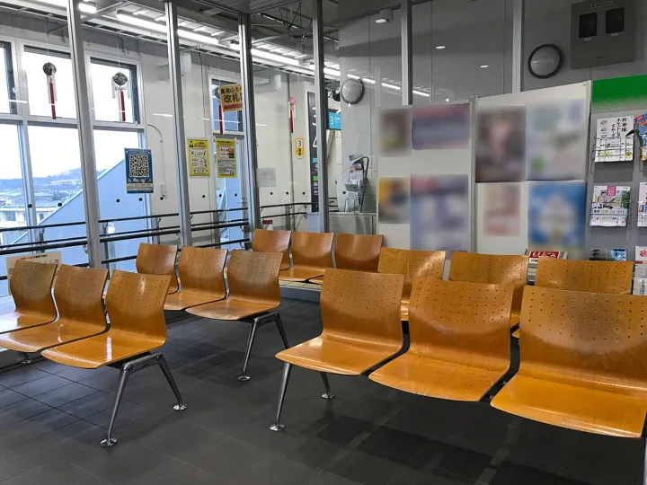 Photo d’origine : Des rangées de sièges de bois vides dans une salle d'attente de gare.
